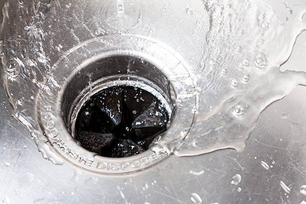 Water flows down the garbage disposal drain in a kitchen sink.